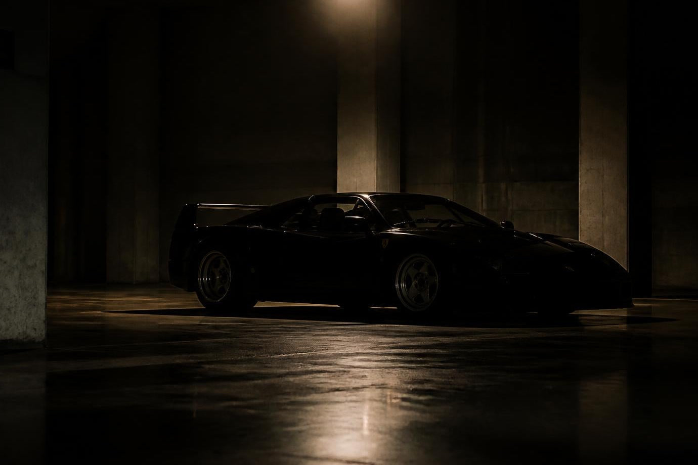 A dark sports car parked inside a dimly lit concrete parking structure, with a single overhead light casting a warm glow on the floor.